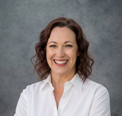 Amanda Rhines-Poehlman, a woman with wavy auburn hair, smiling in a white button-up shirt.